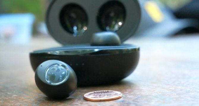 Tranya T10 true wireless in-ear headphones with one earbud in the Qi wireless charging case and one next to a penny for scale