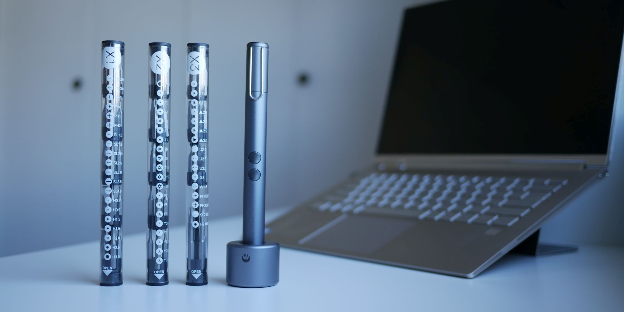 Wowstick and three sets of screw bits standing on a table with laptop in background.