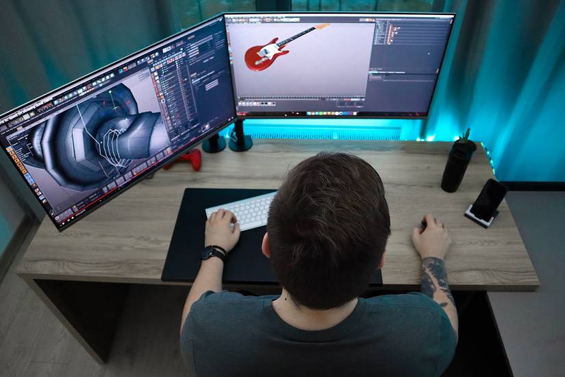 Photo of a man sitting at his computer desk, designing objects using CAD software