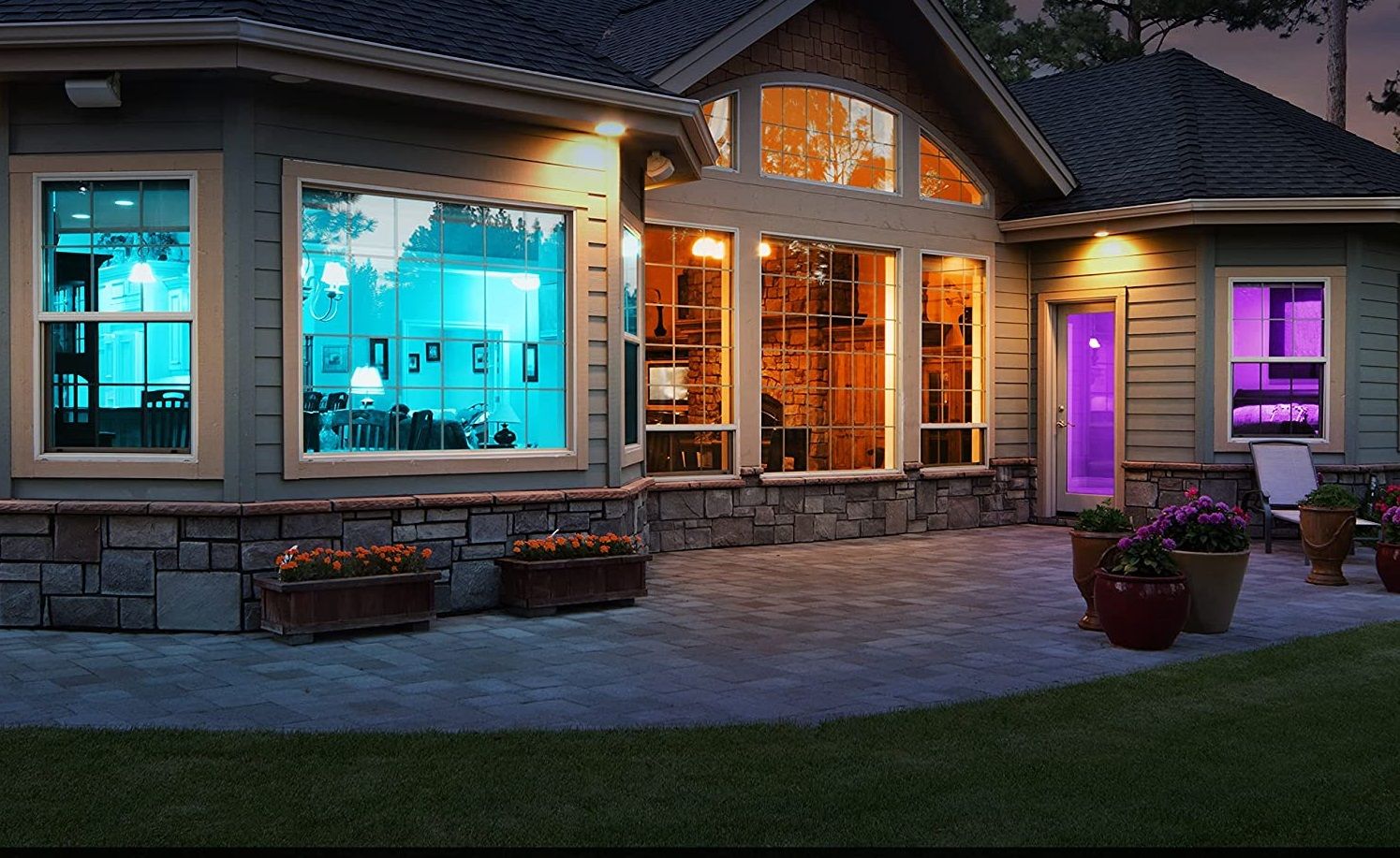 A house viewed from outside with some aqua lighting inside, some warm lighting inside and some purple lighting inside
