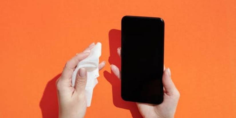 hands holding cloth and black smartphone against orange background