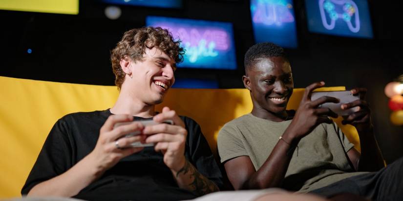 Two guys sat on a sofa playing a game on their mobiles together
