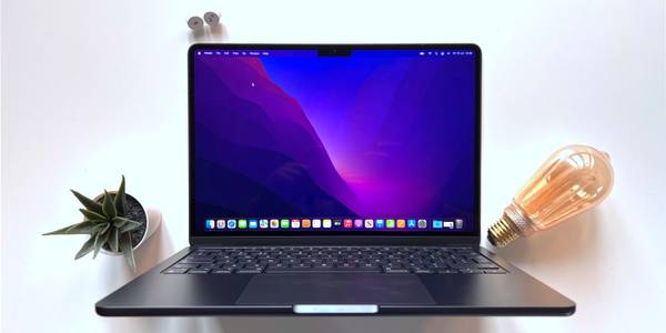 Apple's MacBook Air M2 on a white table, with a light bulb, plant, and the M and 2 keyboard keys around it