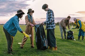 Five people in a grassy field collecting garbage in bin bags