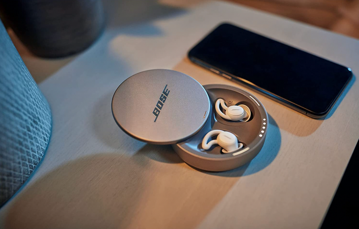 Bose Sleepbuds II در جعبه شارژ روی میز کنار تخت در کنار تلفن هوشمند