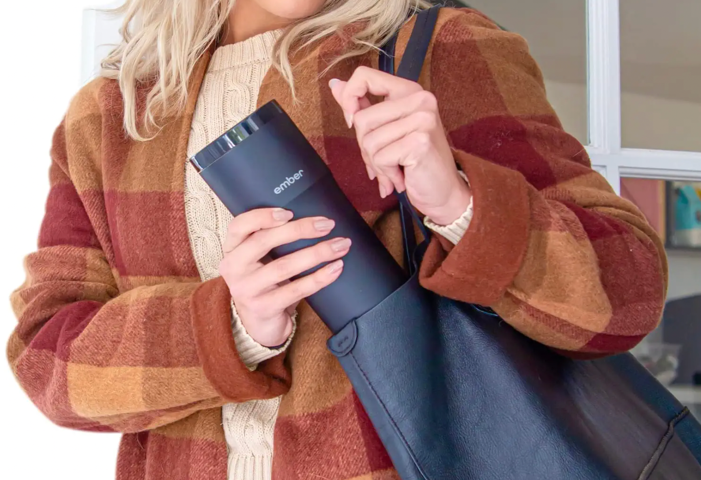 An image showing a woman putting an Ember Temperature Control Travel Mug into her bag