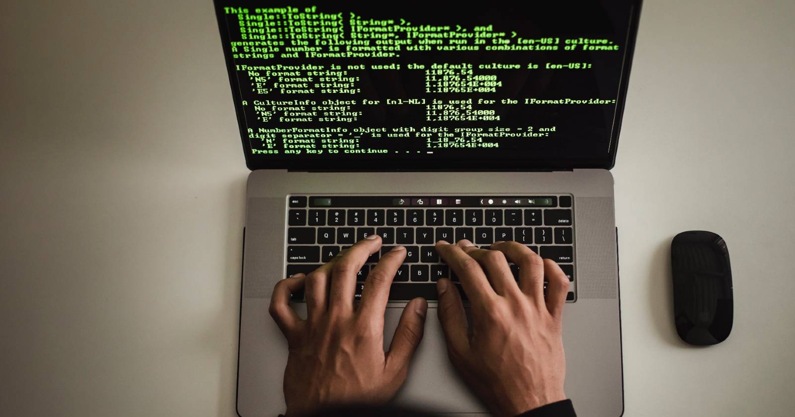 A view from above of hands typing on a laptop with green programming code shown on-screen