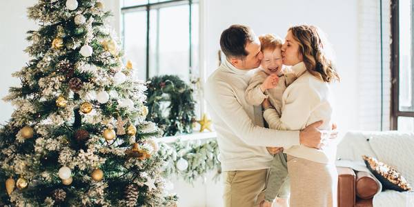 Young family kissing next to Christmas tree.