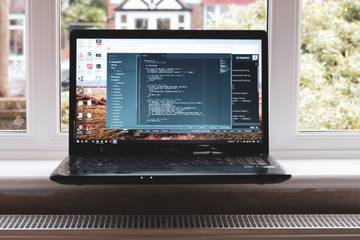 An open laptop sitting on a windowsill with a residential view in the background.