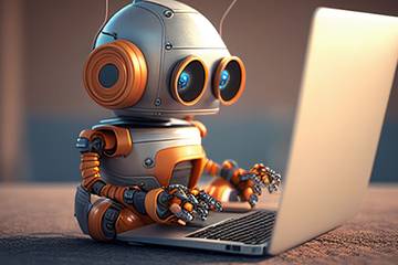 Small orange and silver robot sitting on carpeted floor with a laptop in front of it.