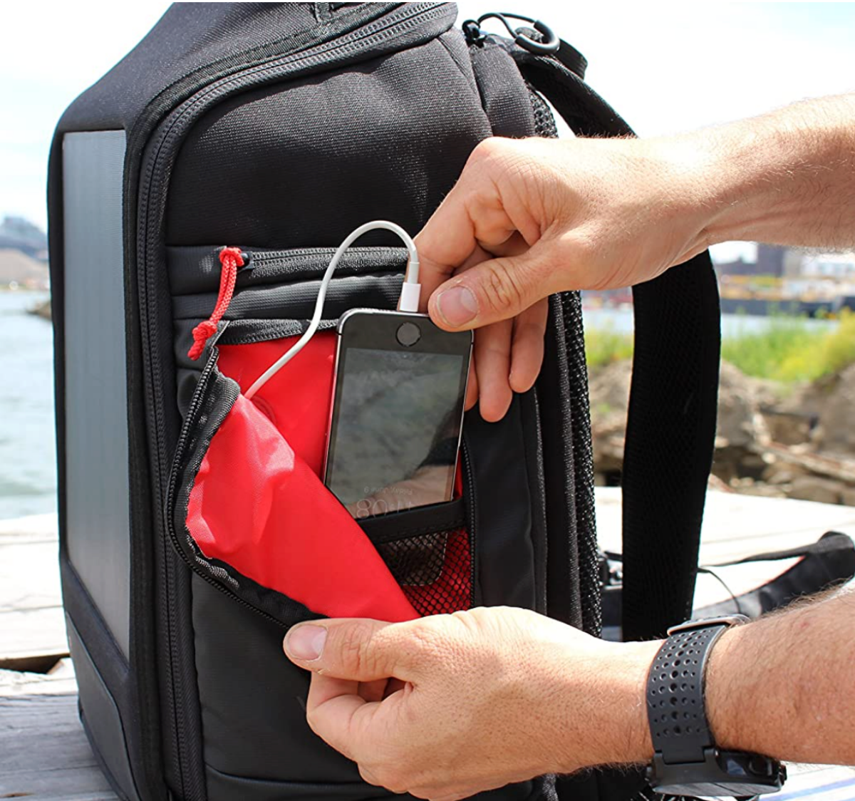 A man charging a smartphone in the side pocket of a Voltaic Systems OffGrid Solar Backpack Charger