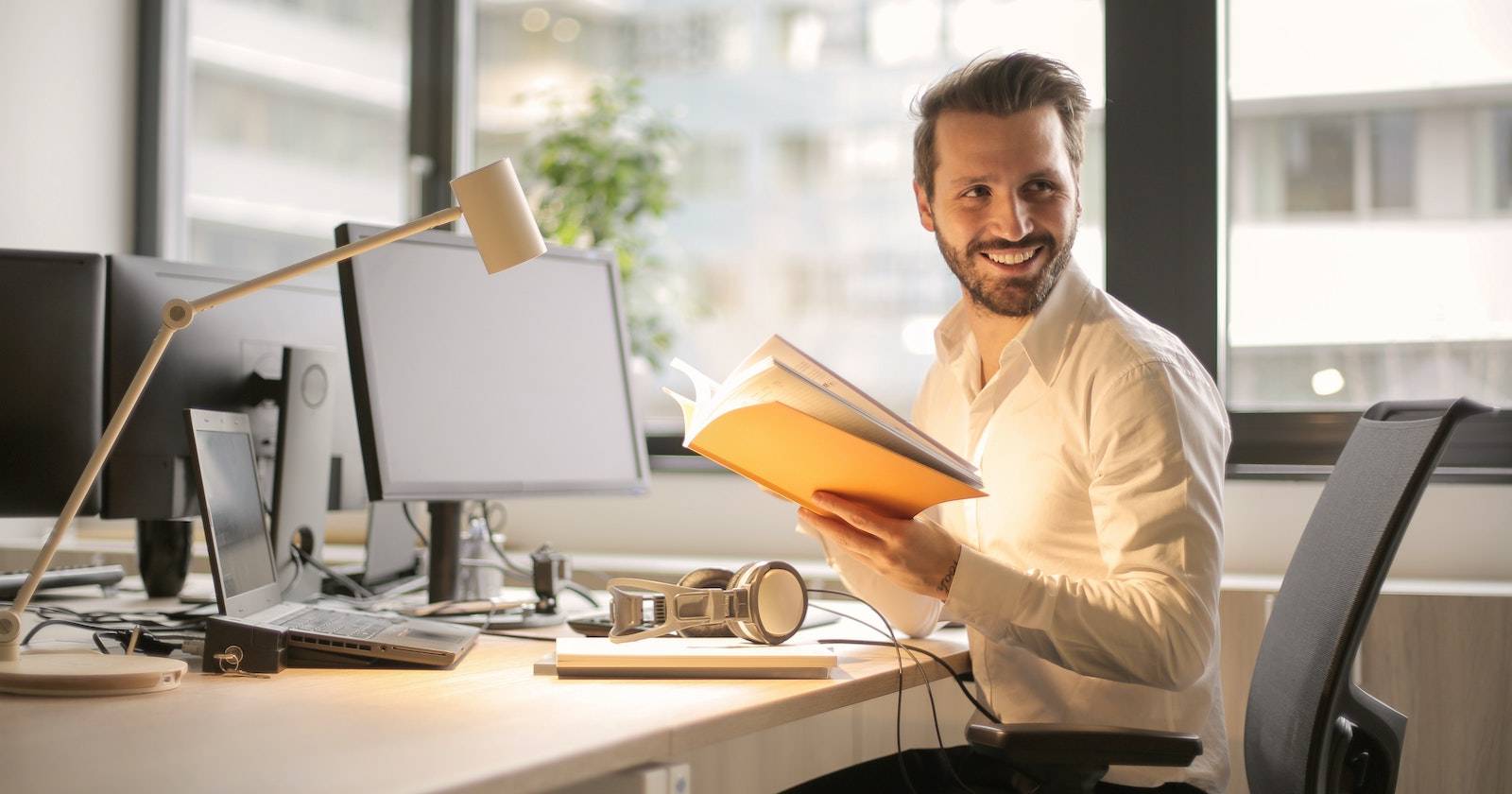 man smiling holding folder in front of computer