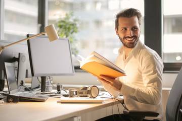 man smiling holding folder in front of computer