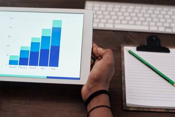 man holding tablet with graphs with writing pad on the table