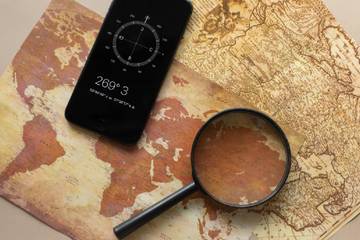 A magnifying glass and a phone display a compass app on top of two old-fashioned maps.