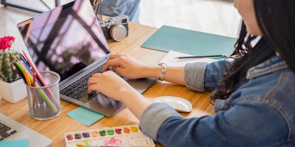 Woman using laptop with art supplies and camera on table