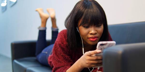 woman lying on sofa using earphones and a smartphone