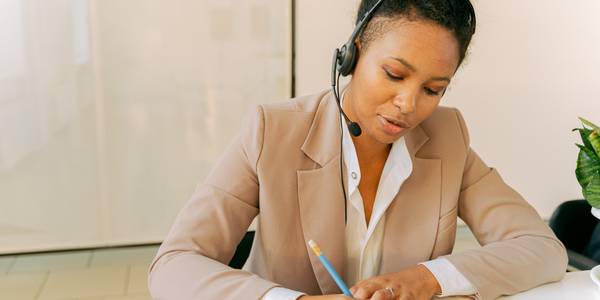 a businesswoman writes while using a headset for a phone call