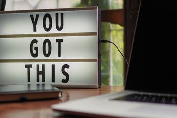a laptop sits unused beside a sign reading YOU GOT THIS