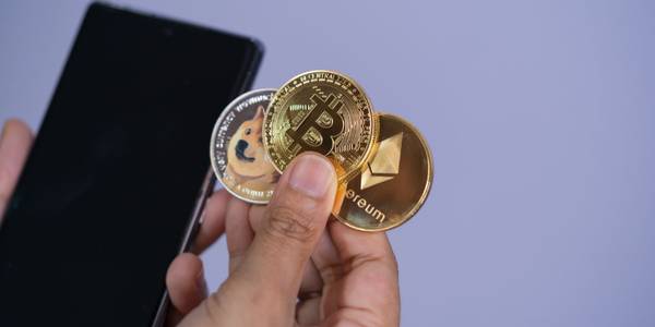 bitcoin ethereum and dogecoin coins in person's hand holding smartphone