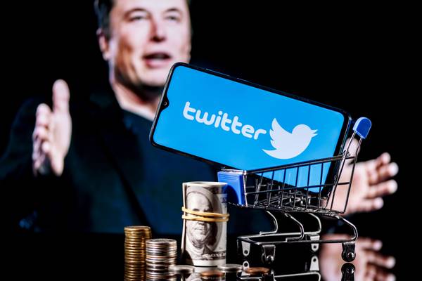 elon musk sitting behind twitter logo on smartphone