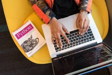 A person programming on a notebook with a Python book on the chair