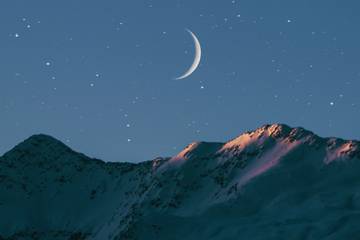 A crescent moon over a mountain at nighttime