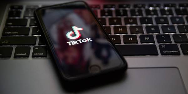 TikTok brand logo on the screen of Apple iPhone 7 with Keyboard of Macbook Pro in background
