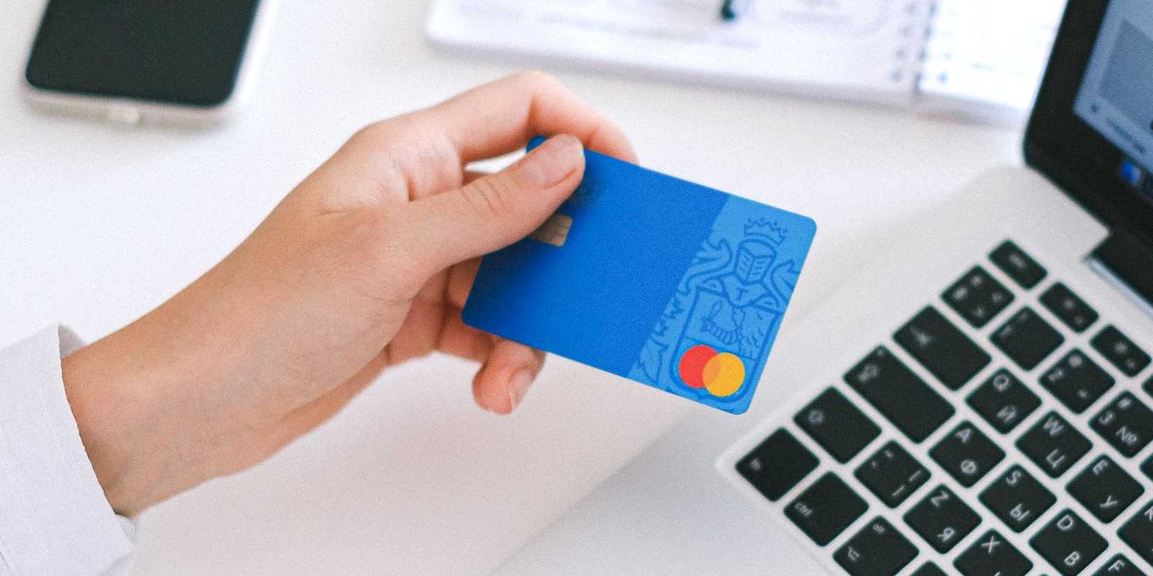 a hand holds a debit card above a laptop keyboard