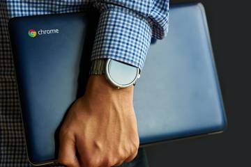 A close-up of a Chromebook being carried with one arm.