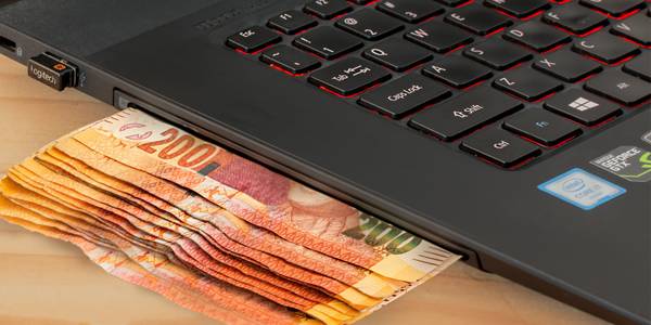 laptop with a pile of notes hiding under it on a wooden table