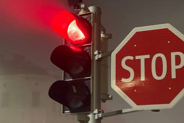 A set of traffic lights showing a red light next to a “STOP” sign