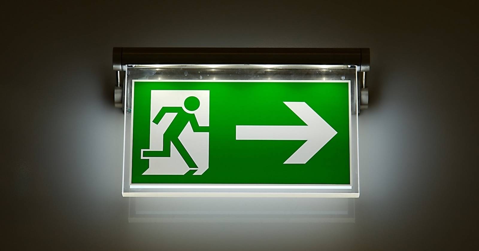 A green and white exit sign shows a stick figure leaving through a door with a large arrow pointing to the right.