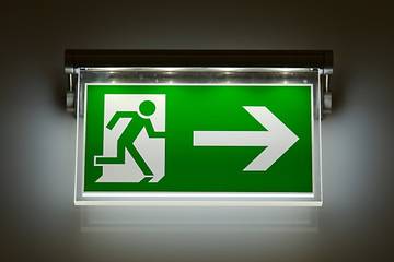 A green and white exit sign shows a stick figure leaving through a door with a large arrow pointing to the right.
