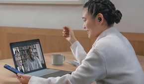 A woman wearing Sony WF-1000XM5 earbuds while chatting on her laptop.