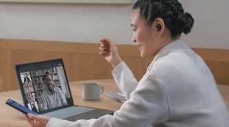 A woman wearing Sony WF-1000XM5 earbuds while chatting on her laptop.