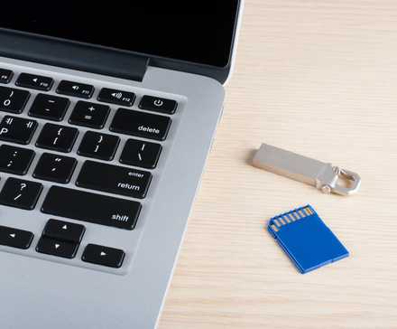 a MacBook next to a USB flash drive and an SD card on the desk