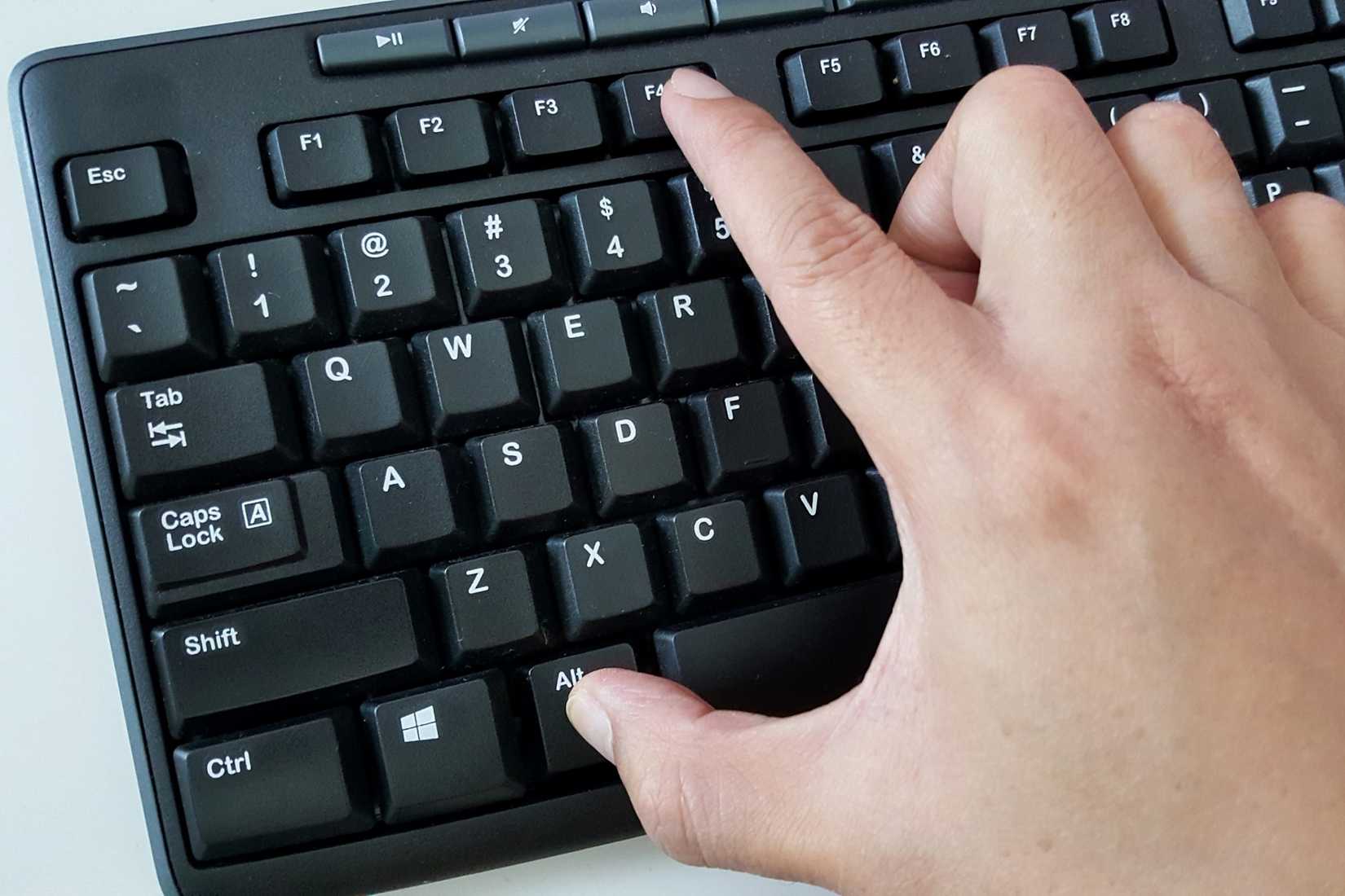 A man pressing the Alt and F4 keys on a Windows keyboard