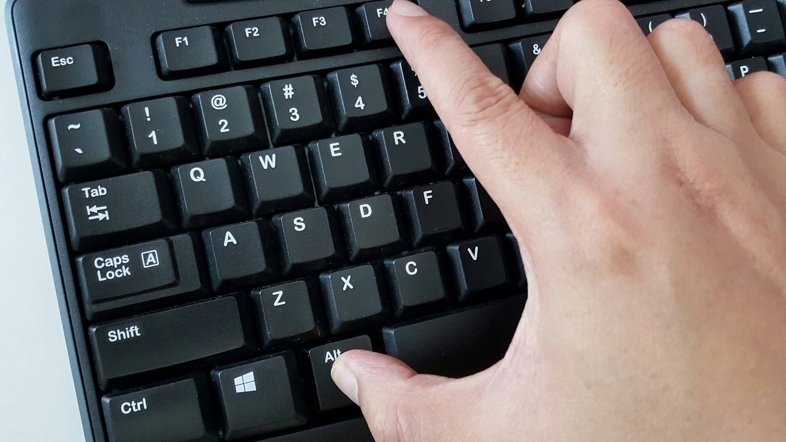 A man pressing the Alt and F4 keys on a Windows keyboard