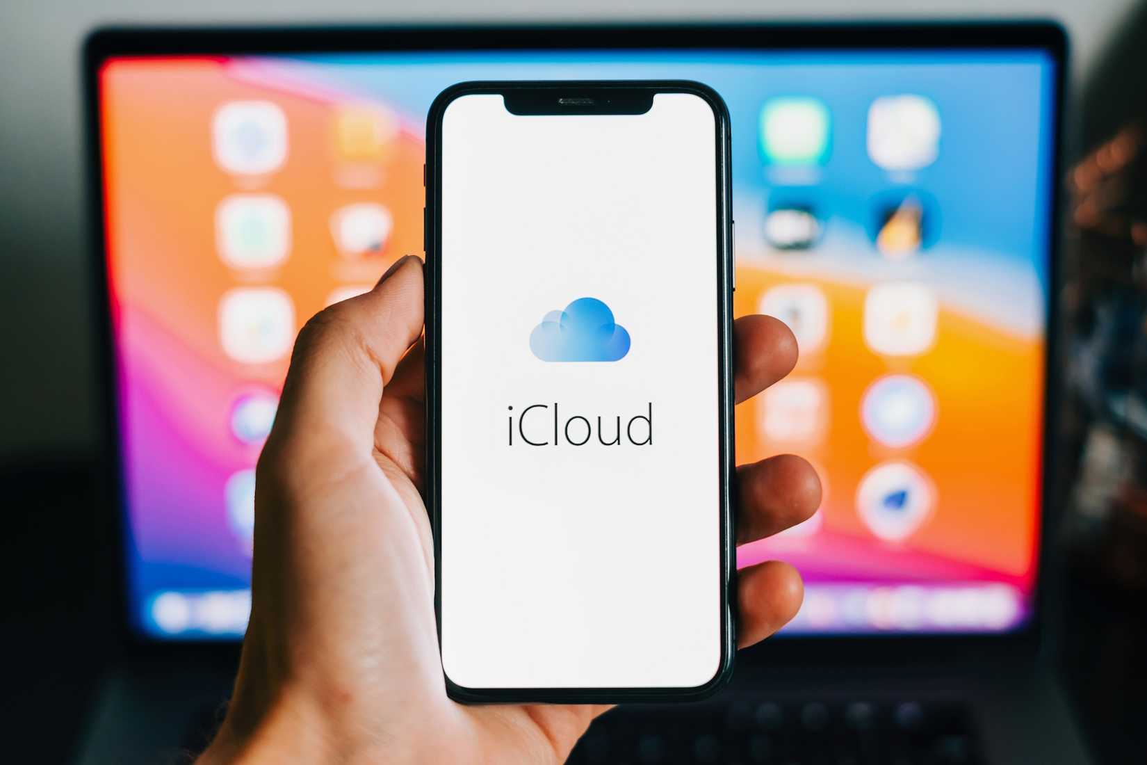 iCloud logo appearing on an iPhone with a MacBook in the background