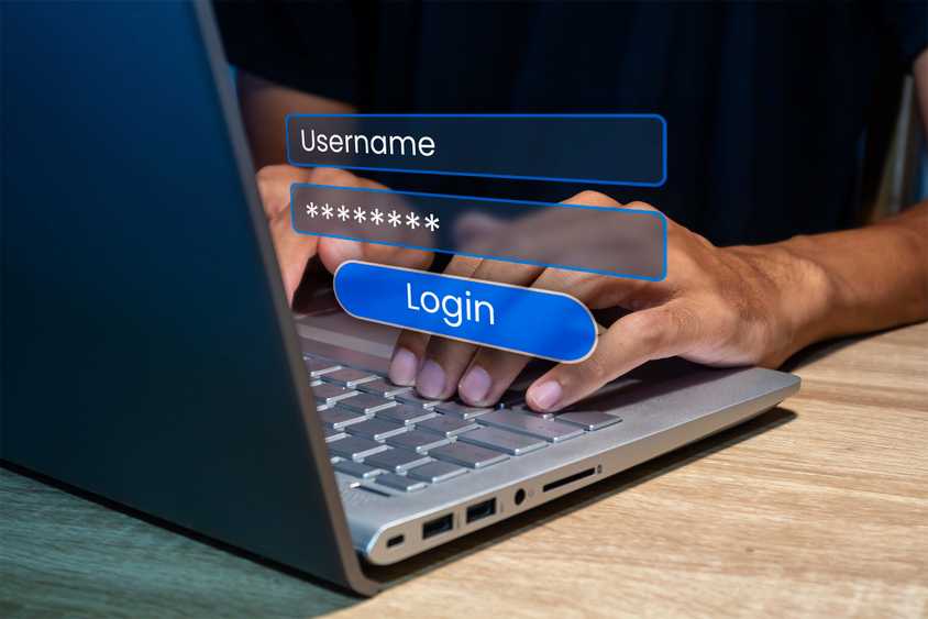 A person using a laptop, typing in a username and password.