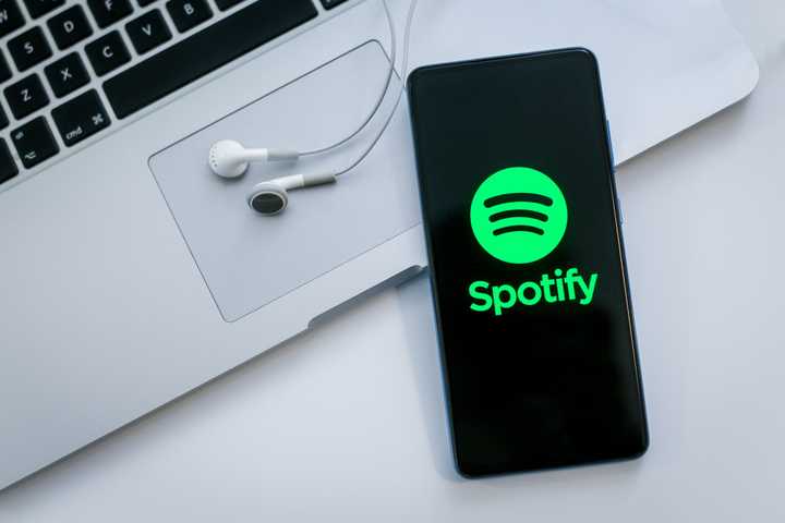 spotify on a smartphone screen with a laptop and earphones in the background