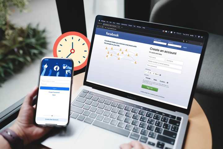 facebook login page on a smartphone and laptop with a clock in the background