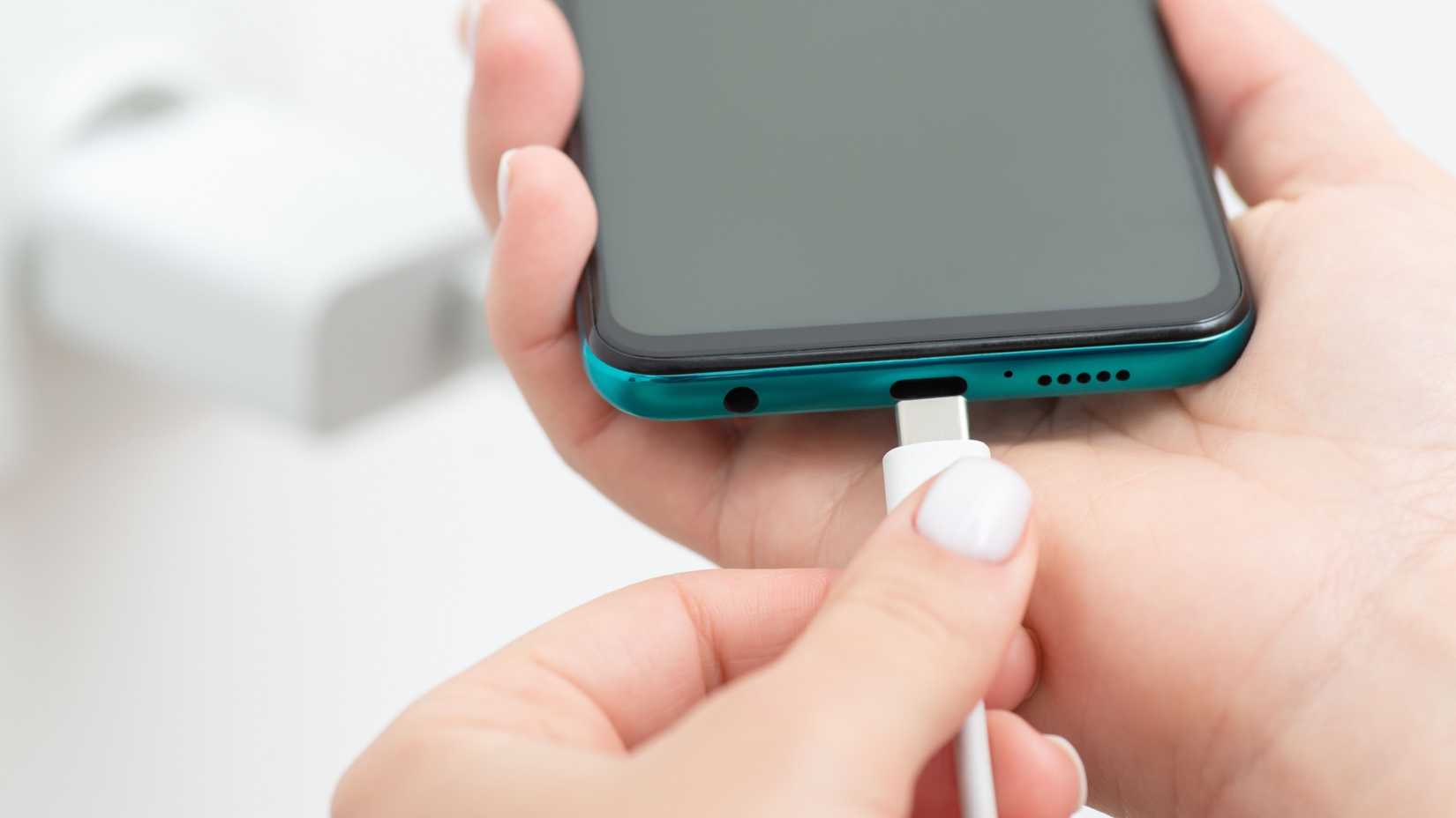 Hand connecting charger to smartphone