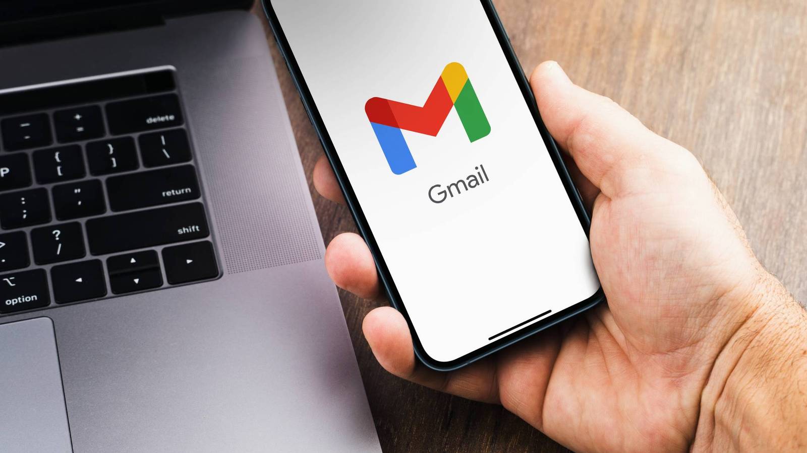 Gmail logo opening on smartphone next to laptop
