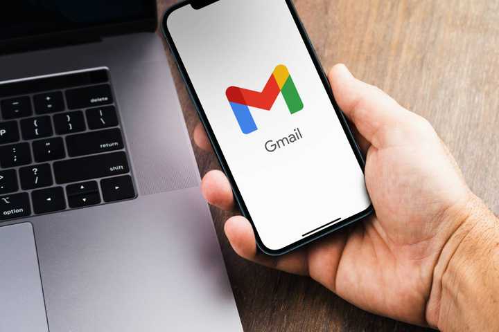 Gmail logo opening on smartphone next to laptop