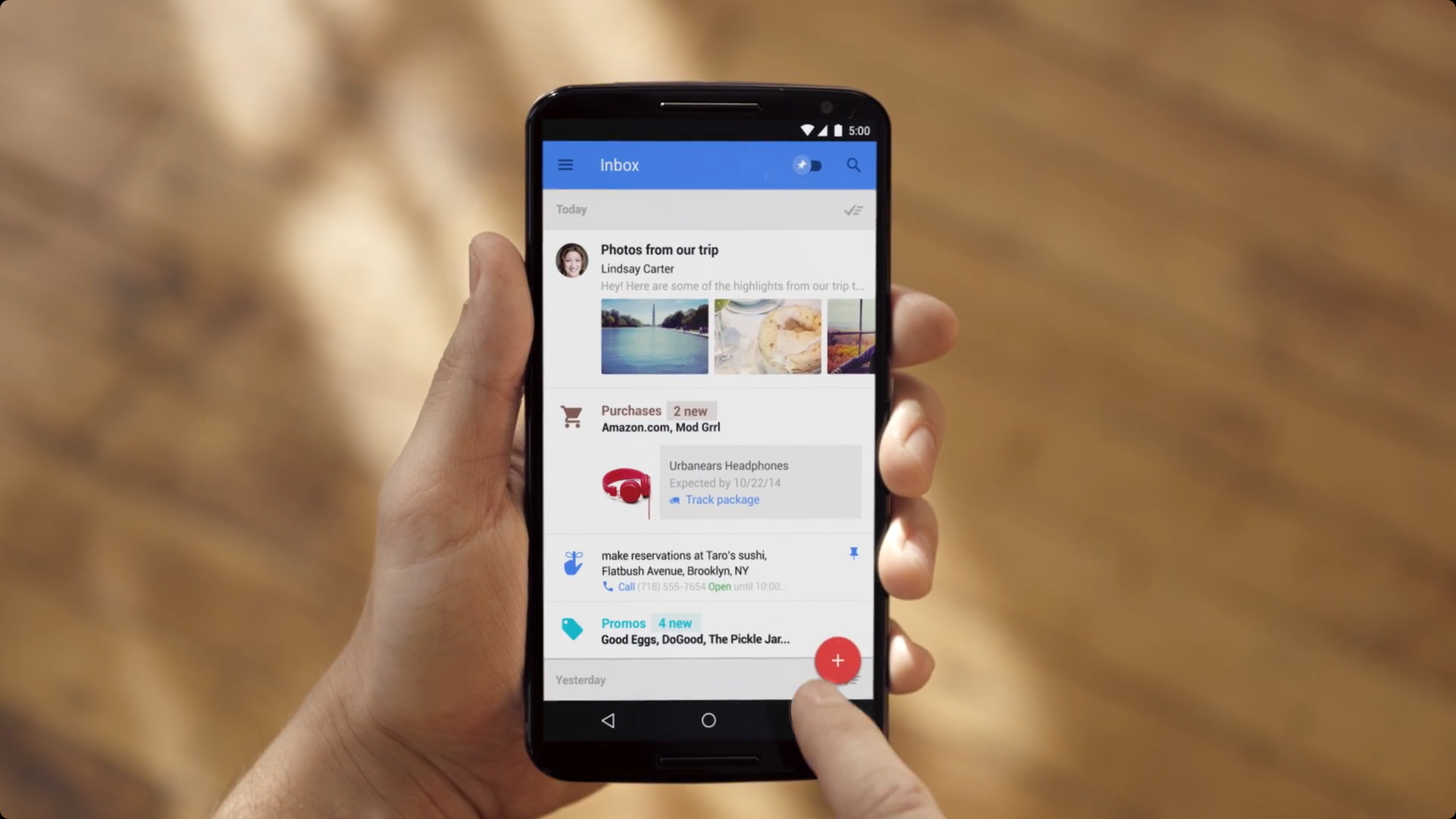 A hand holding a phone showing an inbox by Google with various messages.
