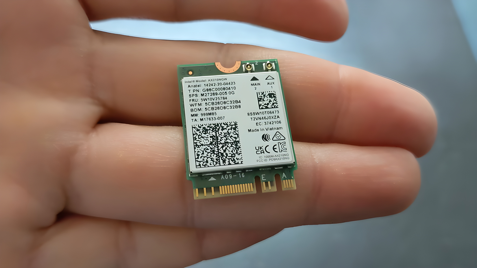 A hand holding a small Intel AX210NGW Wi-Fi module.