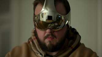 A man in a hoodie wears a reflective metallic visor showing a living room and another person, from Netflix’s 3 Body Problem