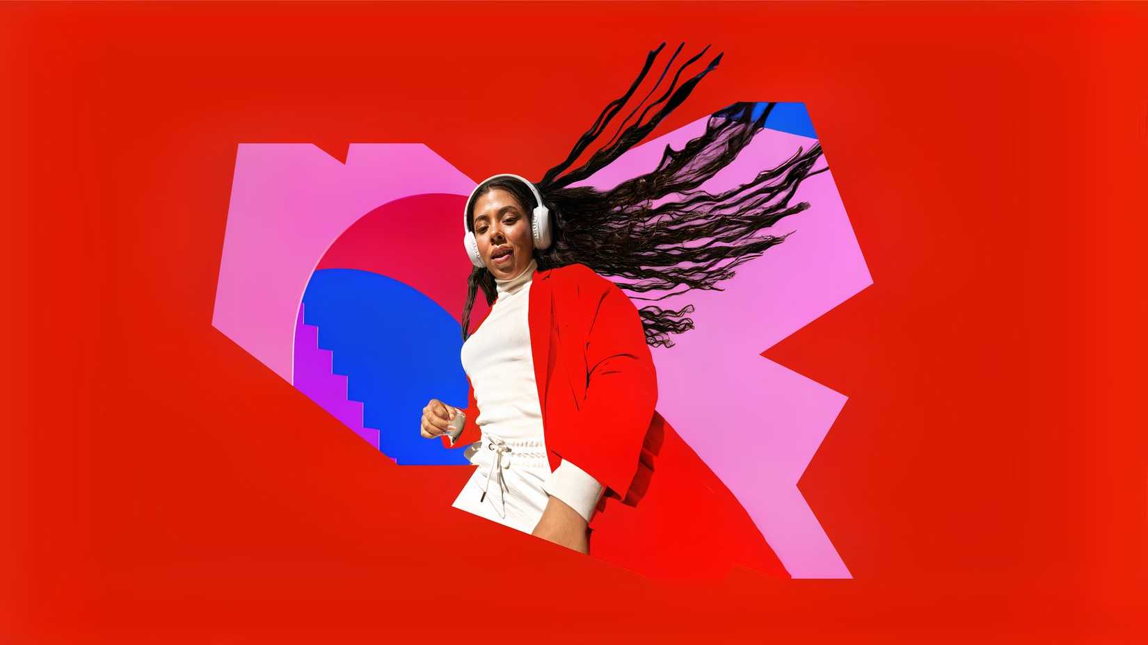 A woman with a white sweater and a red blazer with white headphones on appearing isolated against a background of red, pink, purple, and blue. Her hair is blowing behind her.